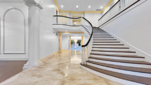 Grand foyer with sweeping staircase in a Beverly Hills estate listed by Hosana Saputra, featuring marble floors, elegant columns, and classic architectural details.