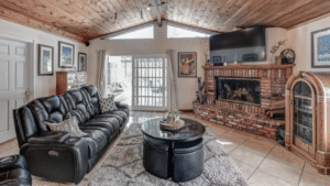 Warm and inviting living room in a Costa Mesa home listed by Mary Kontra, featuring a vaulted wood ceiling, brick fireplace, leather seating, and natural light.