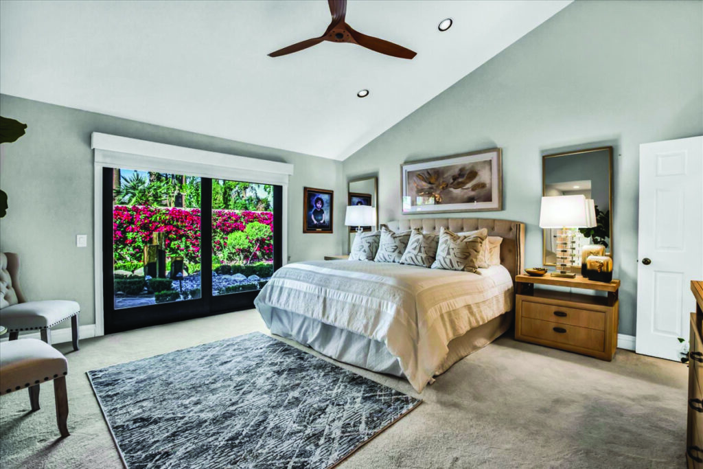 Primary bedroom in a Palm Desert home featuring vaulted ceilings, a ceiling fan, and sliding glass doors opening to a lush private garden, listed by Angela Caliger.