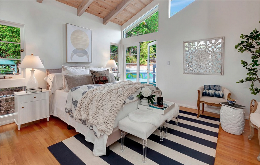 Light-filled bedroom in a Laguna Beach cottage featuring vaulted wood-beam ceilings, hardwood floors, and French doors opening to a lush private outdoor area, listed by Halsey Williams.