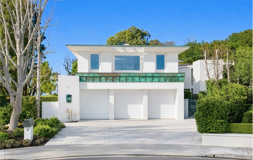 Front exterior view of a modern two-story white luxury home in Newport Beach featuring a three-car garage, copper-patina balcony trim, and lush California landscaping.