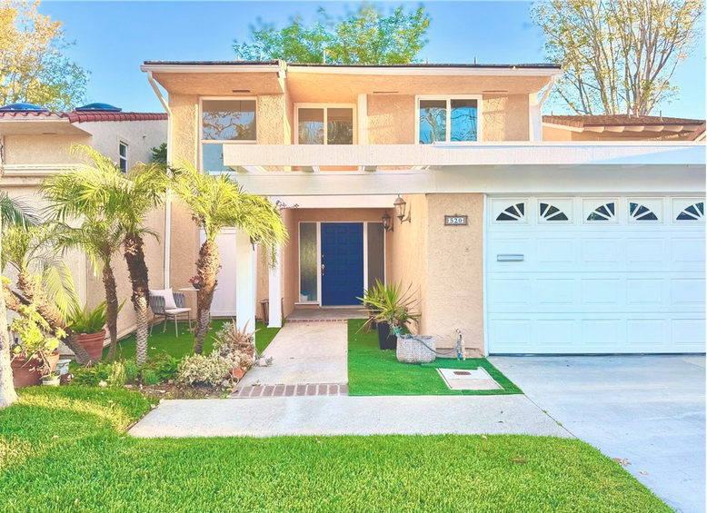 Front exterior of a contemporary white two-story luxury home in Newport Beach featuring a three-car garage, unique green copper-patina balcony trim, and a large second-floor picture window.
