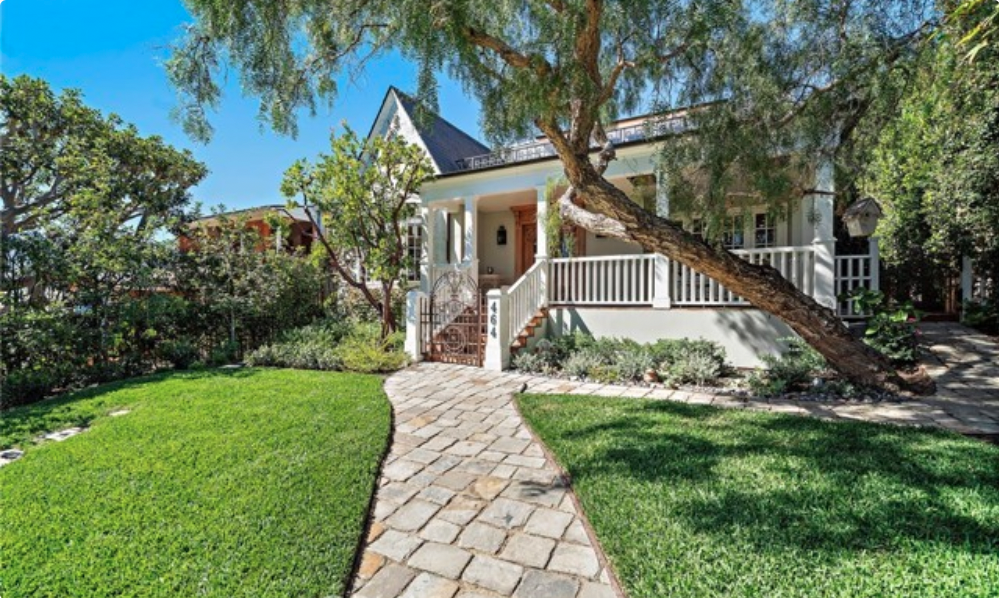 Charming Laguna Beach cottage with a covered front porch, stone walkway, mature trees, and landscaped green lawn.