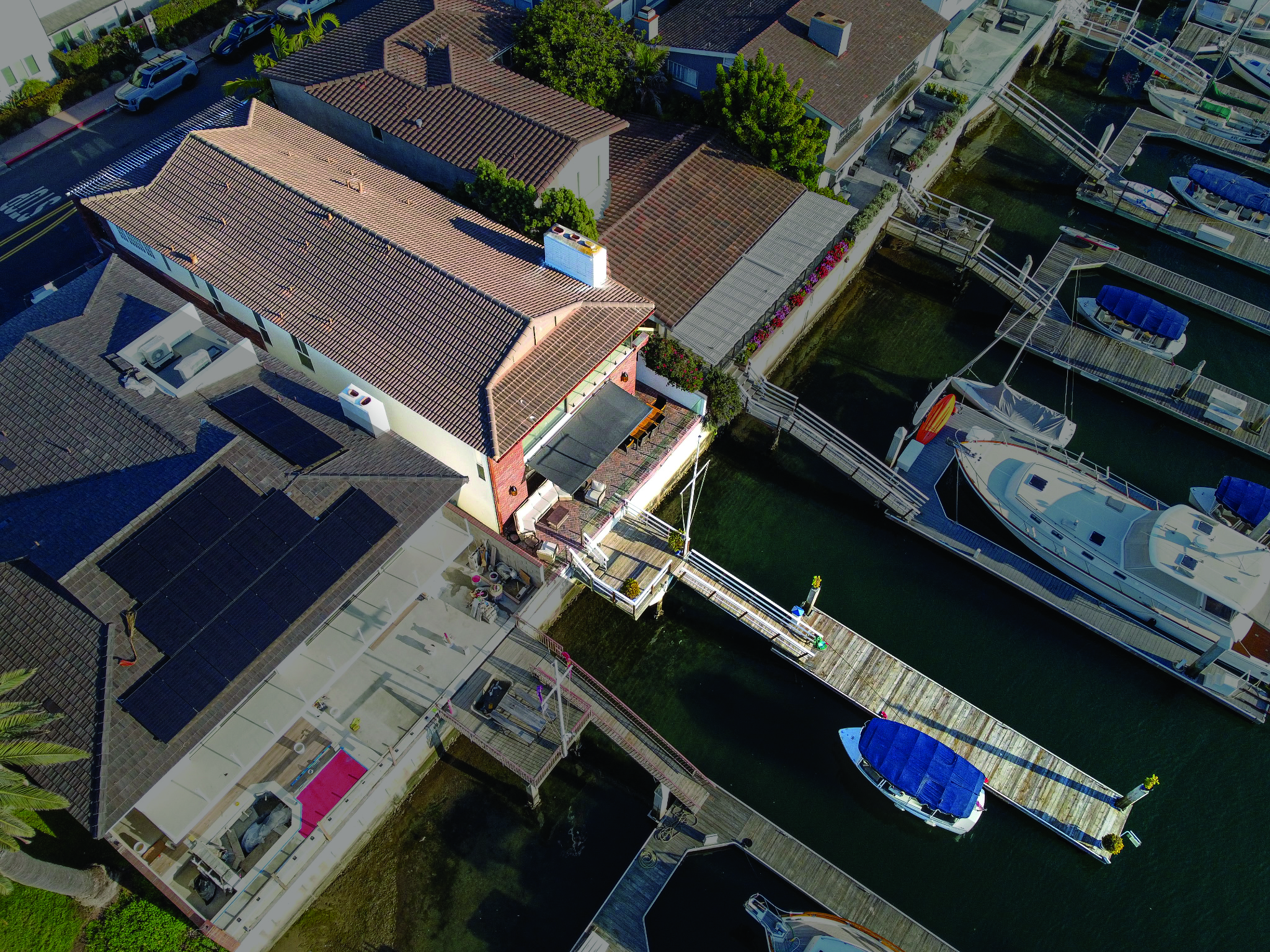 Aerial view of a waterfront home in Newport Beach with a private boat dock extending into the canal, surrounded by neighboring luxury homes and moored yachts.