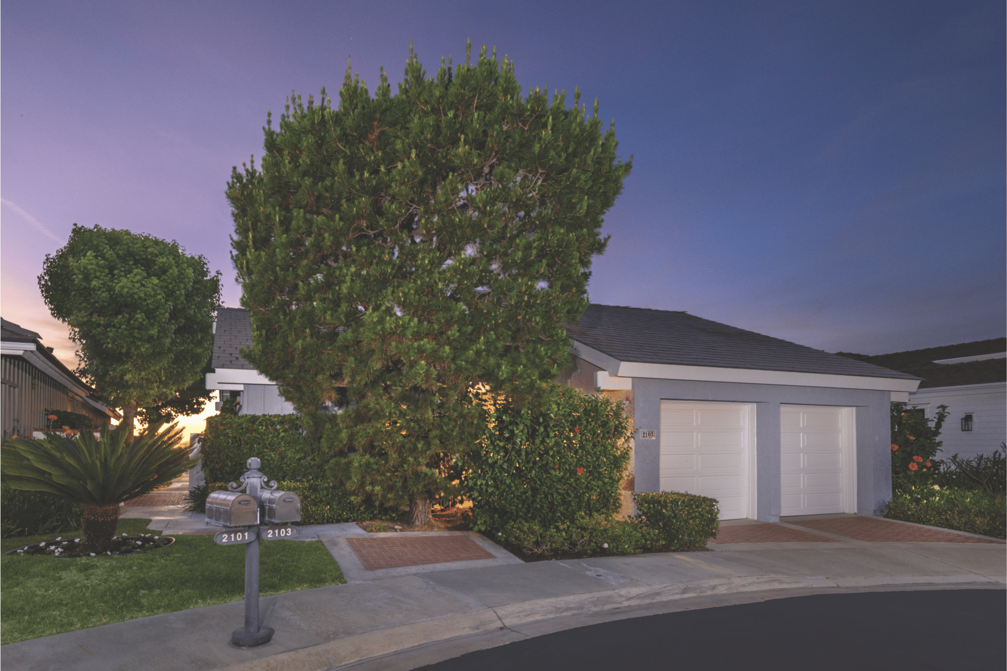Twilight exterior of 2103 Yacht Grayling in Newport Beach, featuring a private driveway, lush landscaping, and attached garage at a coastal Orange County home listed and sold by Anne Hoover.