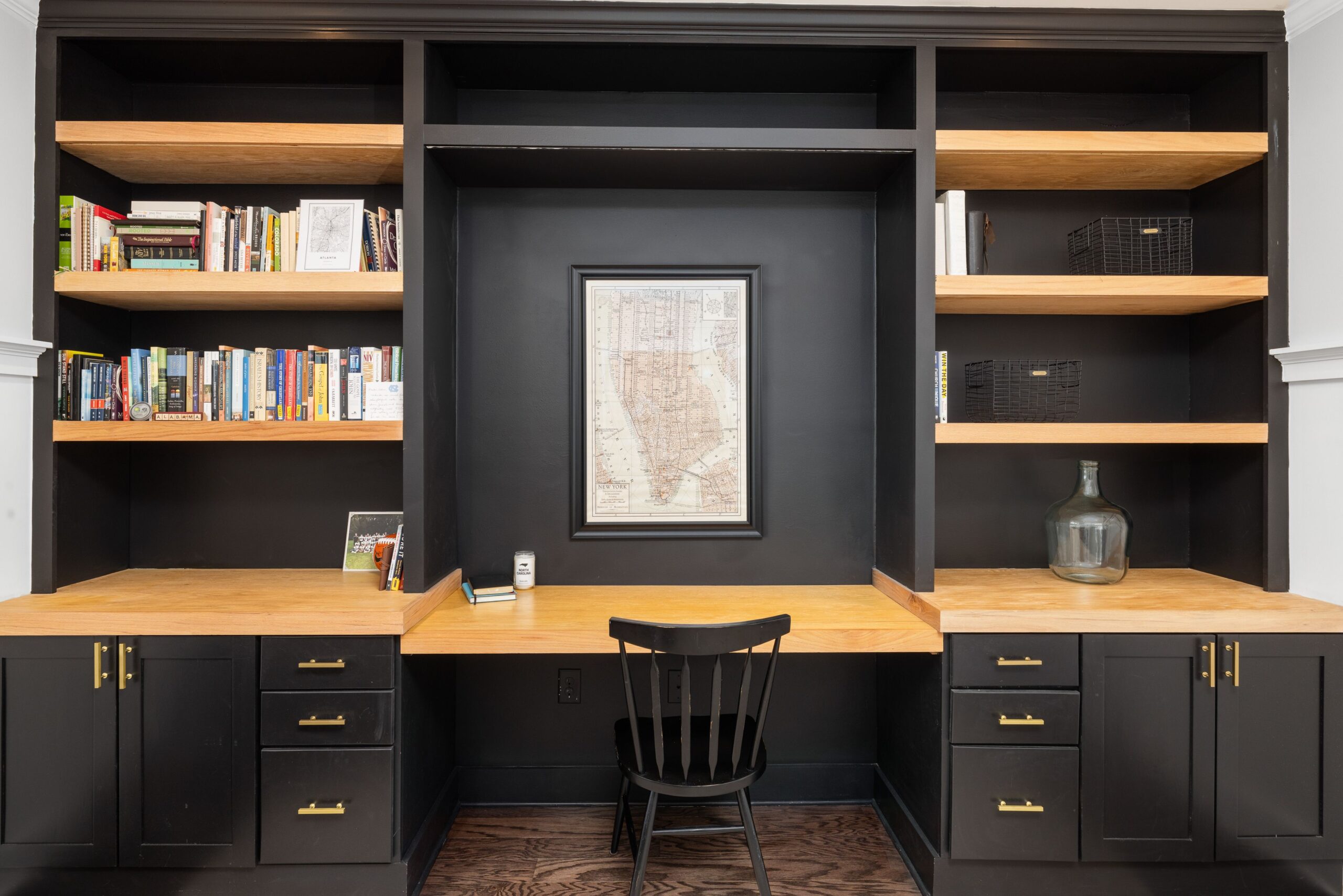 Modern black built-in office desk and study nook with warm wooden counter, open bookshelves, and a framed map.