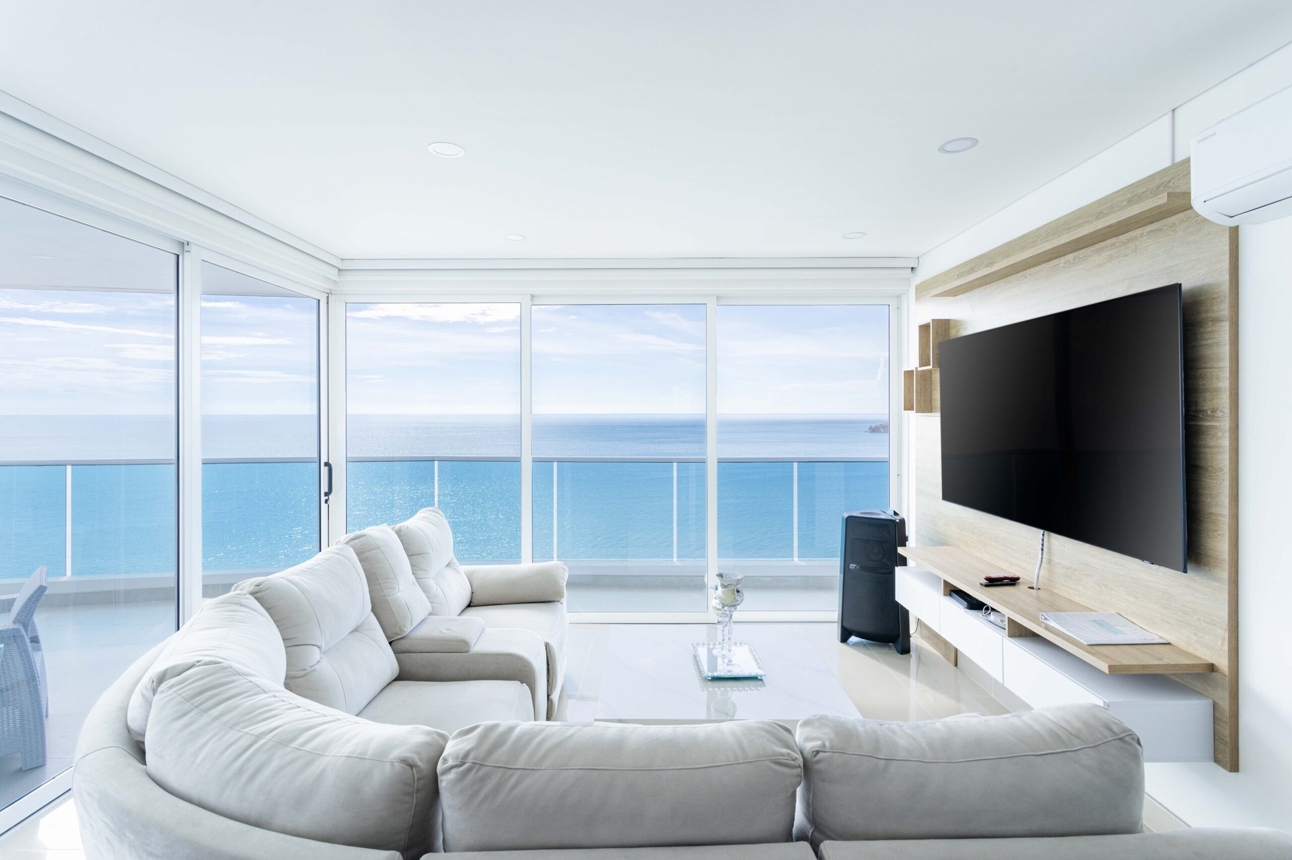 Bright oceanfront living room with floor-to-ceiling windows, modern furnishings, and panoramic coastal views.