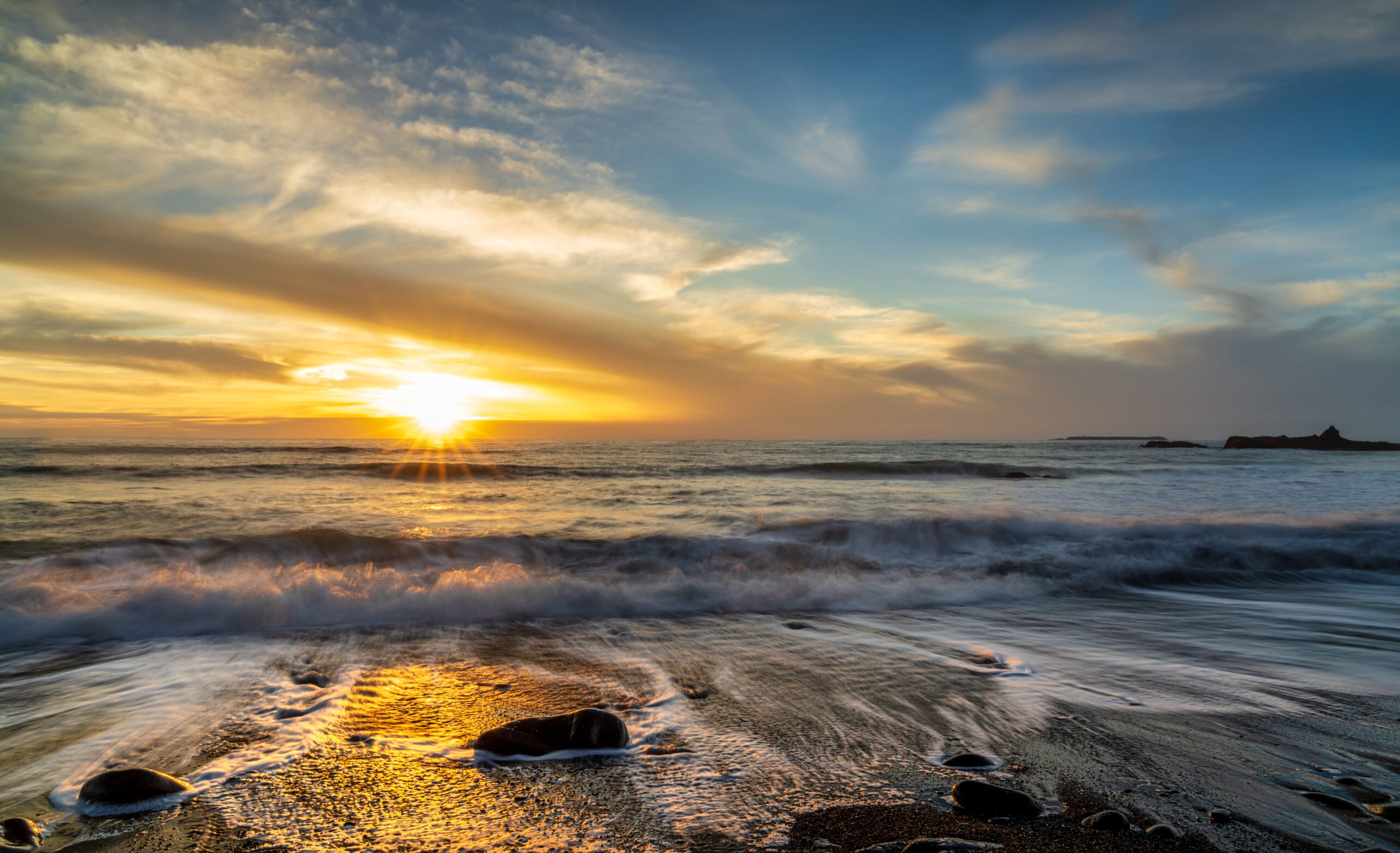 Golden sunset over the Pacific Ocean in Orange County, California, with waves rolling onto a rocky beach.