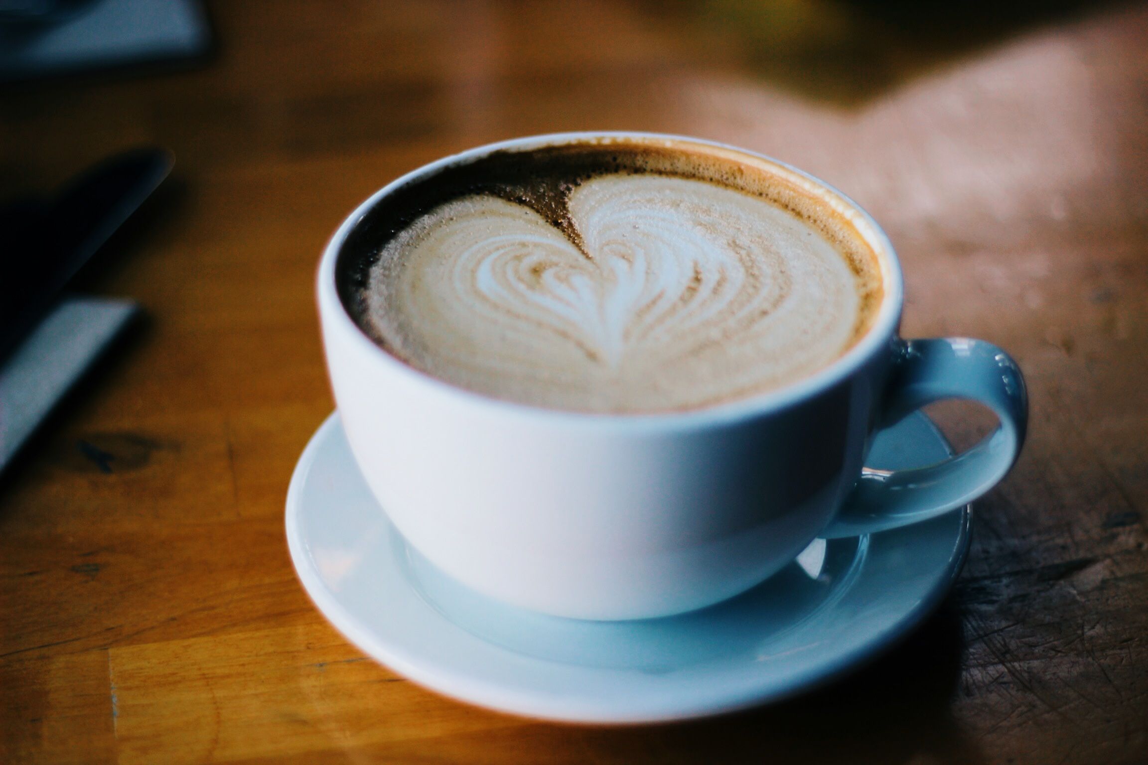 White ceramic cup of coffee with heart-shaped latte art on a wooden café table.