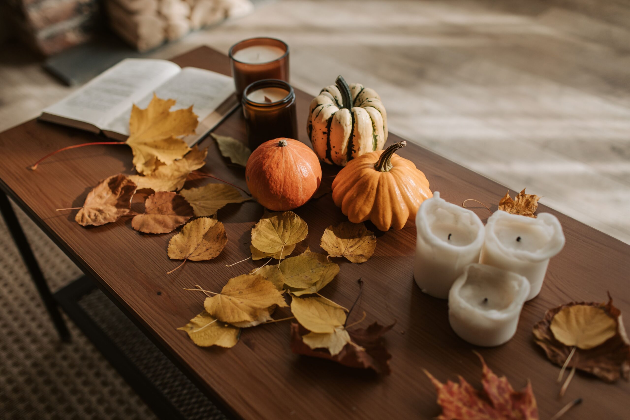 Autumn home décor with pumpkins, candles, fall leaves, and an open book arranged on a wooden coffee table.