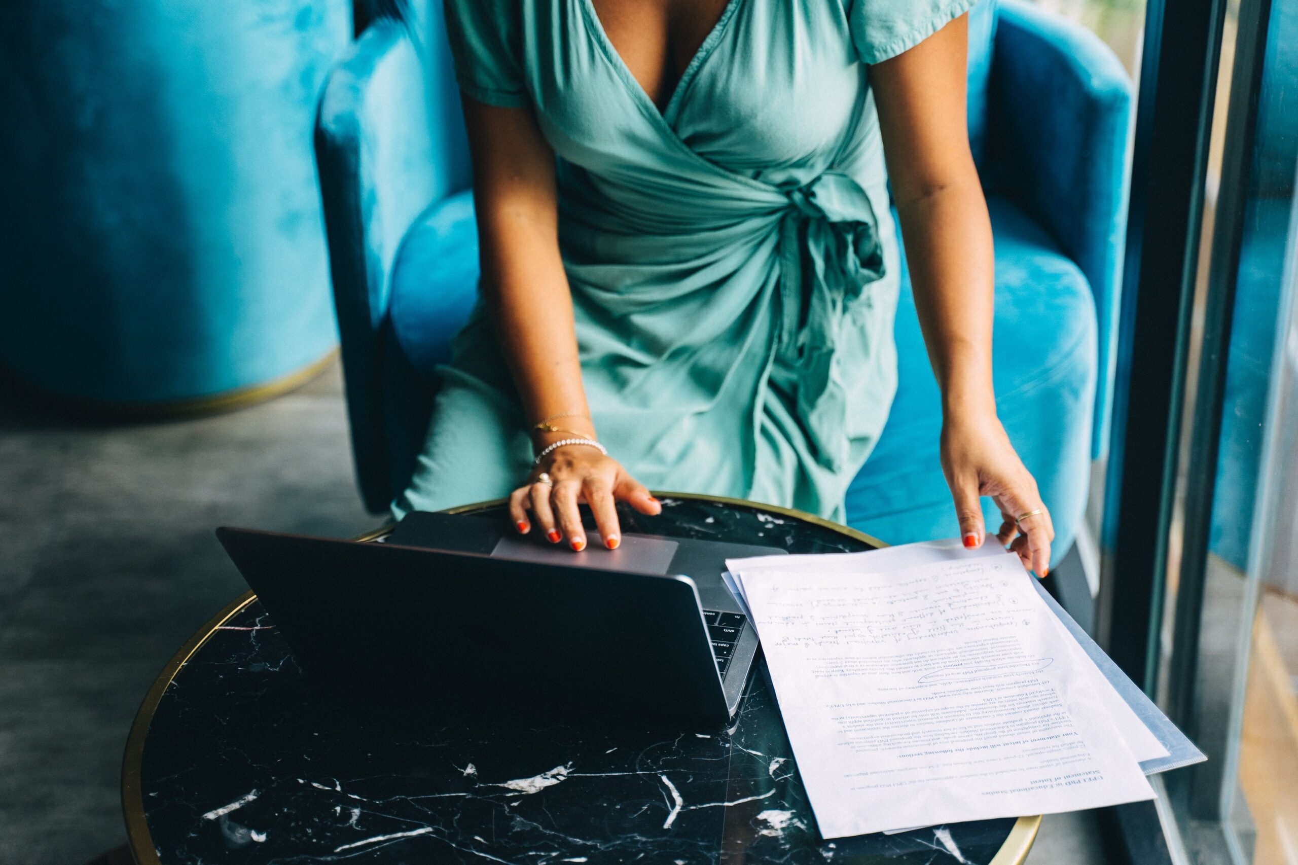 Woman reviewing documents beside an open laptop at a table, representing real estate investment research and financial planning.