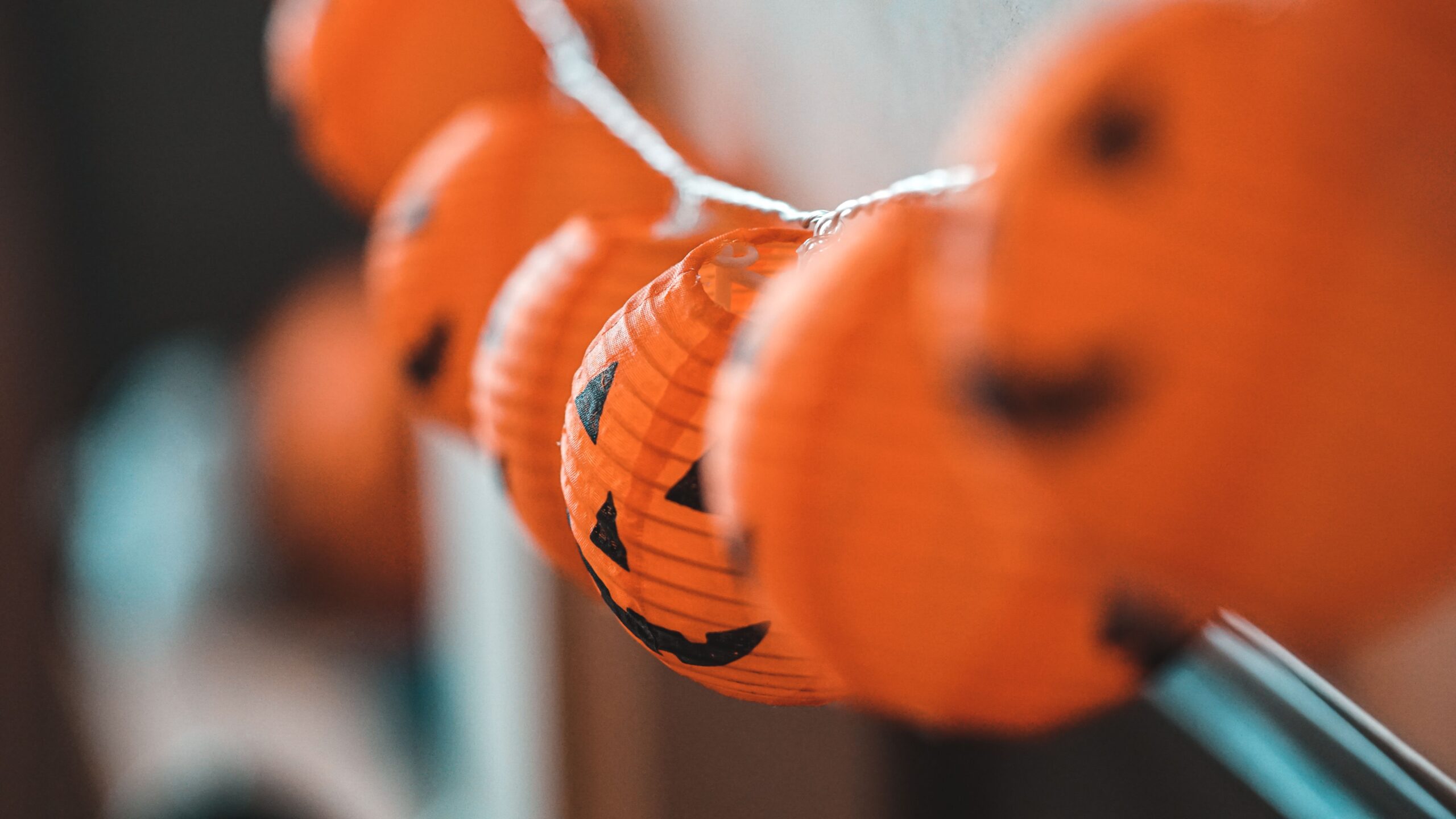 Orange jack-o’-lantern string lights with smiling pumpkin faces glowing against a softly blurred background.